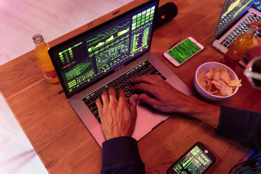 Hands typing on a laptop with coding, phone on desk, symbolizing cybersecurity.