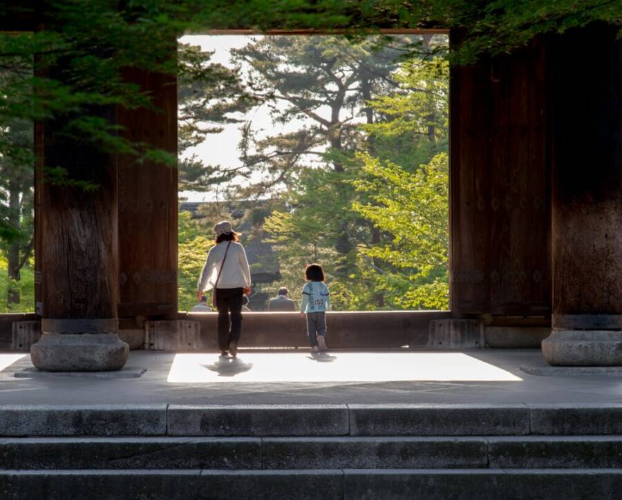 A family strolling through a temple gate surrounded by lush greenery in Kyoto, Japan