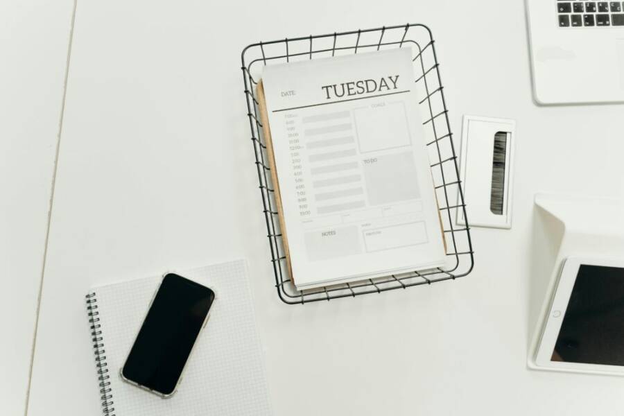 Top view of a neat office desk with a Tuesday planner, smartphone, and gadgets, perfect for scheduling and organization