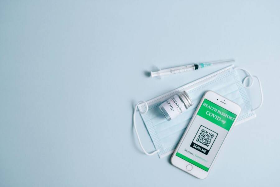 Top view of Covid-19 health passport on smartphone with vaccine, syringe, and mask on blue background